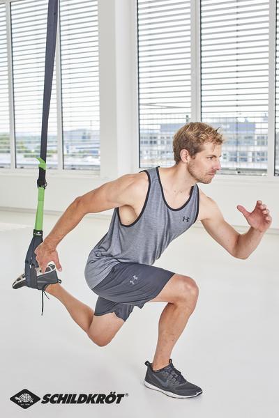 Mann trainiert mit TRX-Bändern im Fitnessstudio, führt Ausfallschritt-Übung aus.