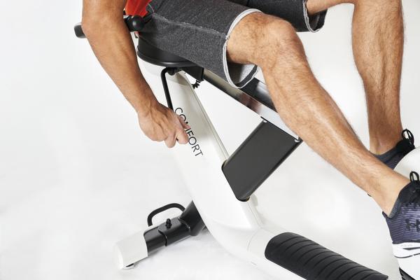 Mann stellt Sitzhöhe an modernem weißen Fitnessgerät für Heimtraining ein.