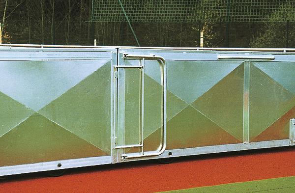 Metallzaun mit integriertem Tor auf einem roten Sportplatz mit grünem Netz im Hintergrund.