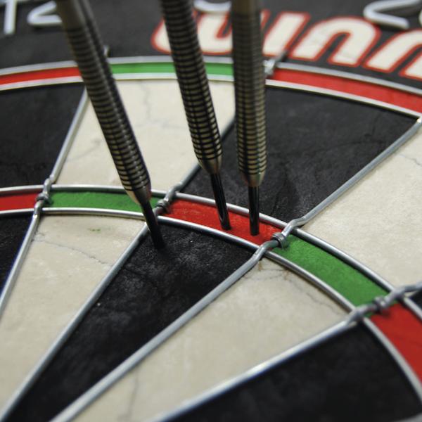 Dartscheibe mit drei Pfeilen, die im Triple-20-Feld stecken, Nahaufnahme.