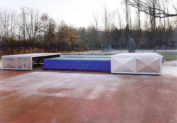 Hochsprunganlage mit Matte und Metallrahmen auf rotem Sportplatz im Freien.