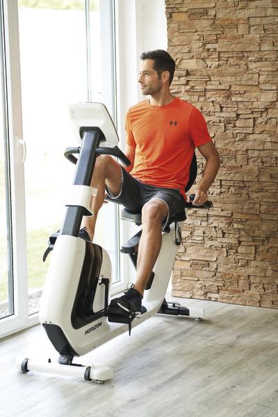 Mann trainiert auf Heimtrainer vor Fenster in modernem Raum mit Steinwand.