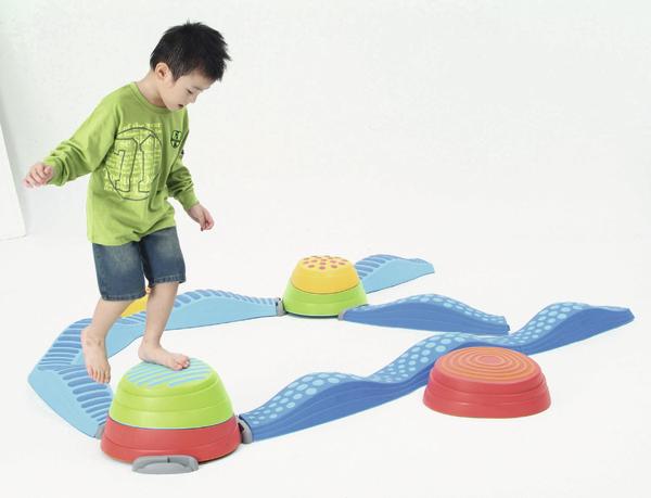 Kind balanciert auf buntem Balancier-Spielgerät aus Kunststoff auf weißem Hintergrund.