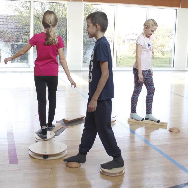 Kinder balancieren auf Holzscheiben und -balken in einer Turnhalle bei Bewegungstraining.