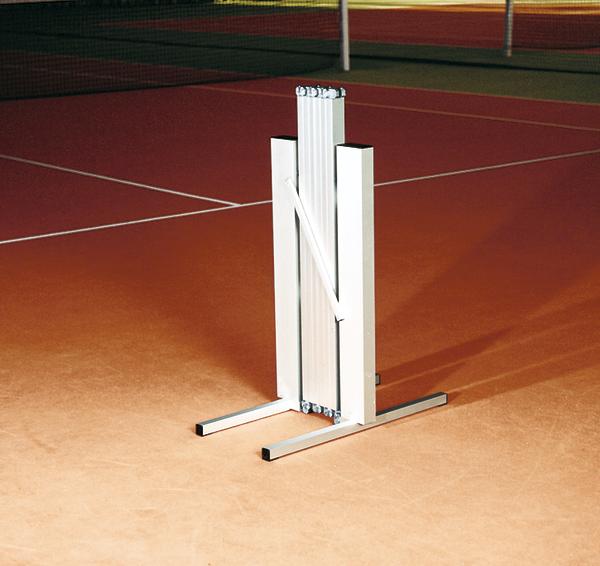 Zusammengeklappter Tennisnetzpfosten auf rotem Tennisplatz bei Nacht.