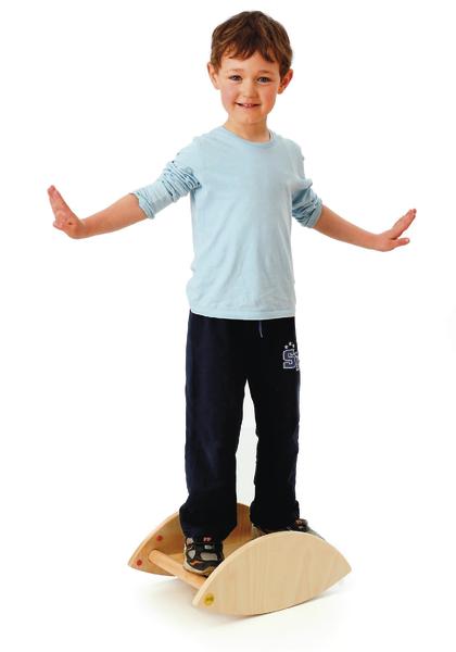 Junge balanciert auf einem Holz-Wippbrett, trägt blaues Shirt und schwarze Hose.