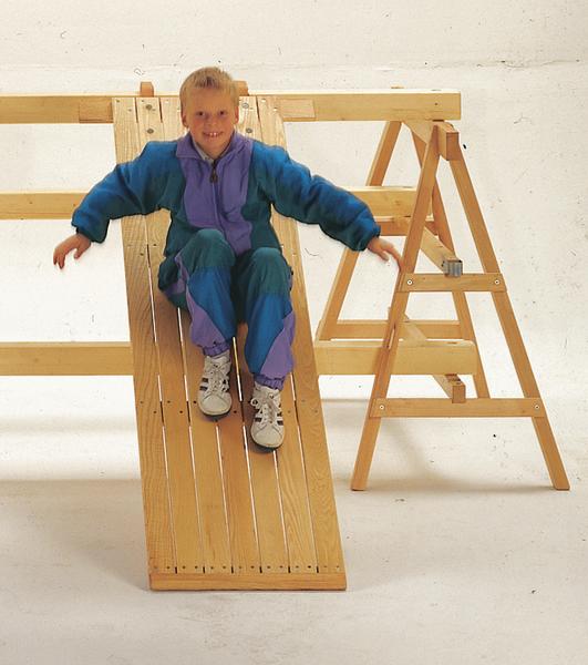 Kind rutscht auf selbstgebauter Holzrutsche mit Leiter in heller Umgebung.