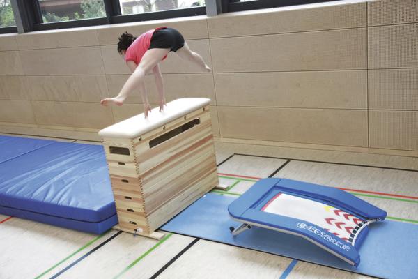Kind turnt im Sportstudio über einen Sprungkasten mit Anlaufmatte und Sprungbrett.