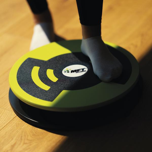 Balance-Board mit Füßen in Socken auf Holzfußboden für Gleichgewichtstraining.