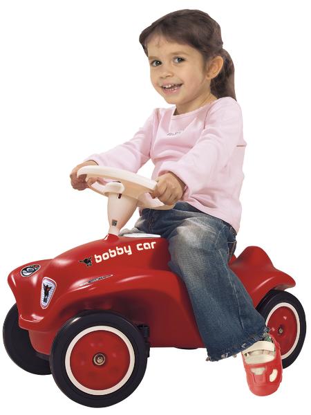 Kind fährt roten Bobby Car Spielzeugwagen, lächelnd, weißer Hintergrund, Kinderfahrzeug Spaß