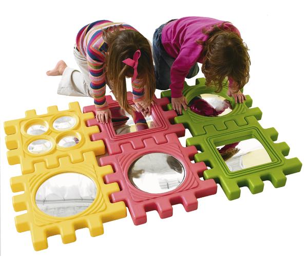 Zwei Kinder spielen mit bunten Spiegel-Puzzleteilen auf weißem Hintergrund.