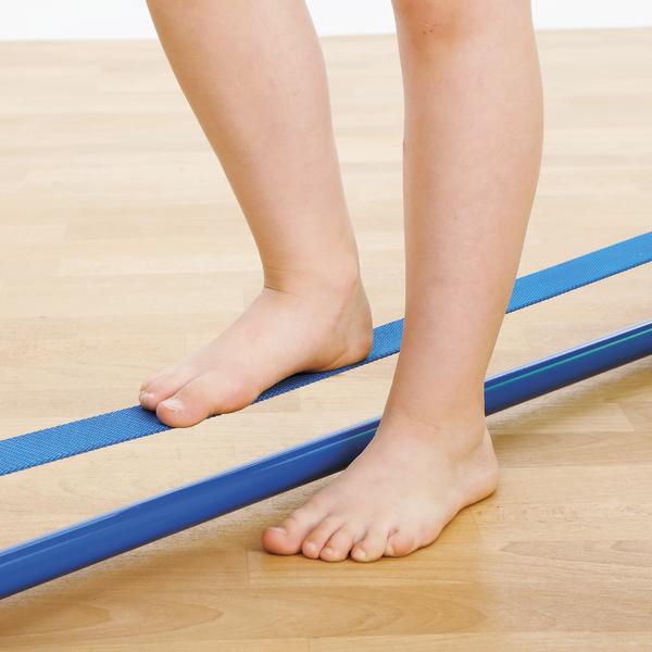 Barfußes Kind balanciert auf einer blauen Slackline auf hellem Holzboden.