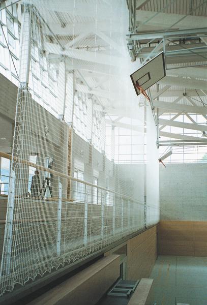 Leere Sporthalle mit Basketballkorb und Schutznetz an der Seitenwand bei Tageslicht.
