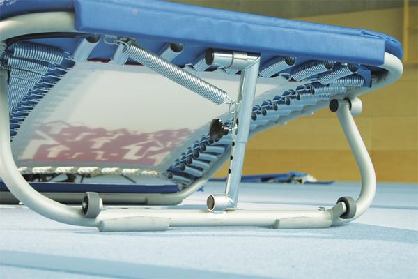 Trampolin mit blauer Umrandung und Metallrahmen auf Sporthallenboden.