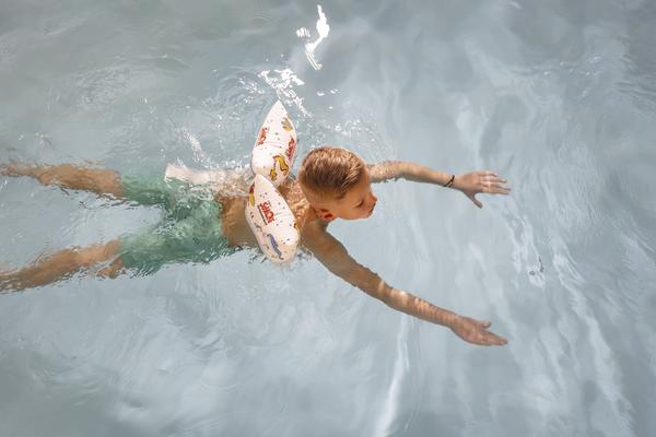 Junge mit Schwimmhilfe schwimmt entspannt im klaren Poolwasser.