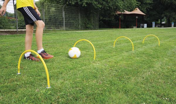 Junge trainiert Fußball-Dribbling mit Hürden auf grünem Rasen im Freien.