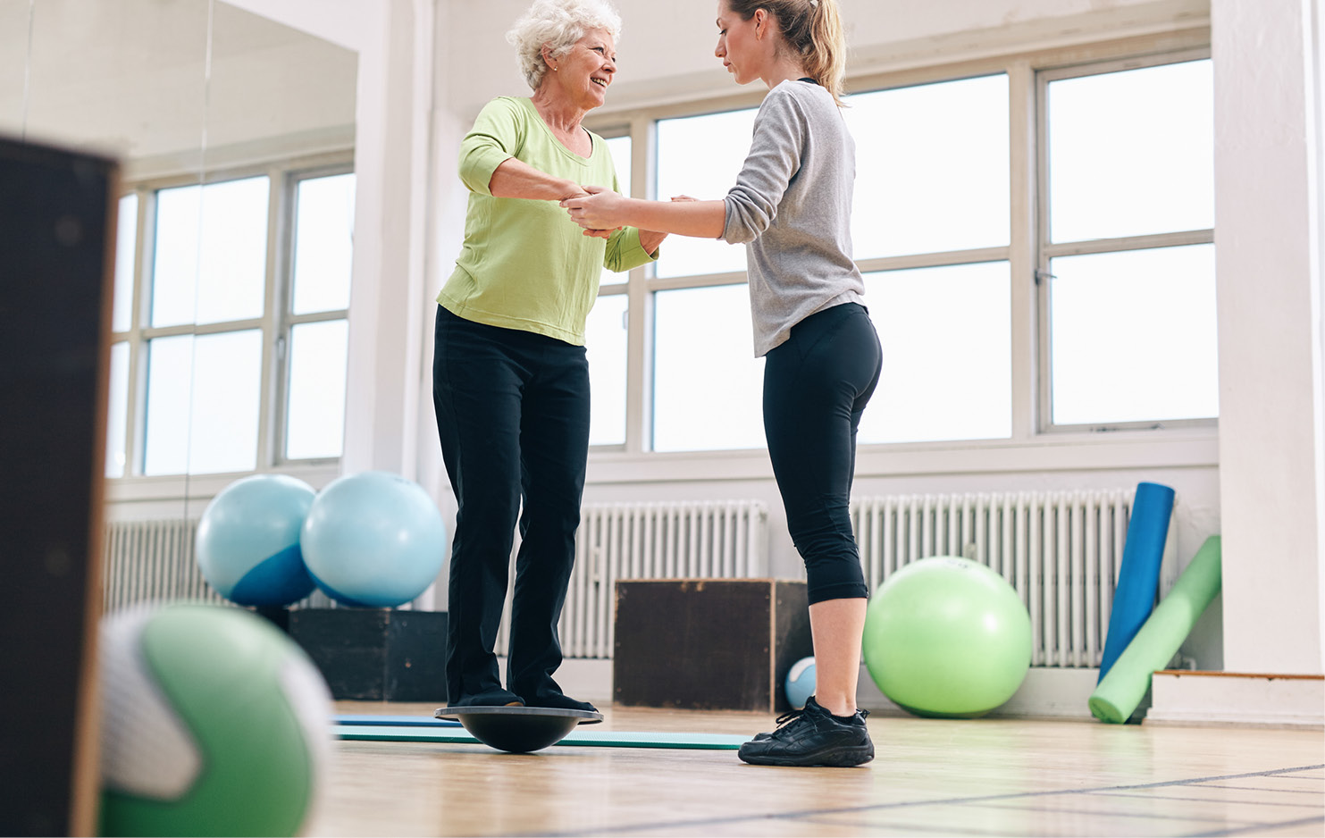 Frau steht auf Kreisel und wird von Therapeutin unterstützt