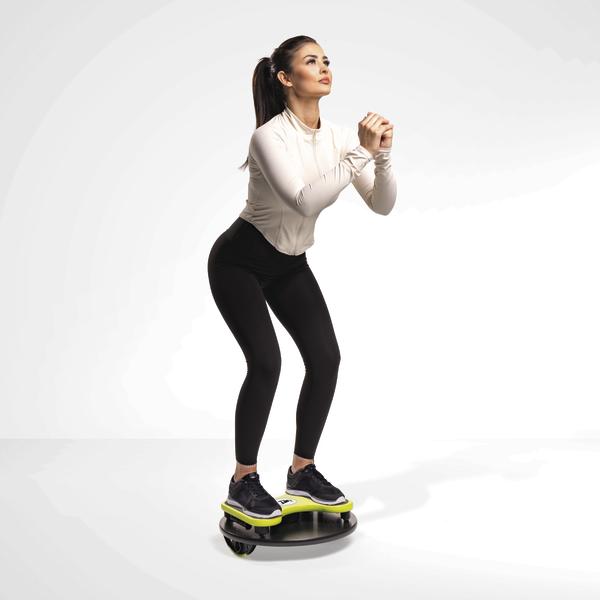 Frau trainiert Balance und Koordination auf einem Wackelbrett in Sportkleidung vor weißem Hintergrund.