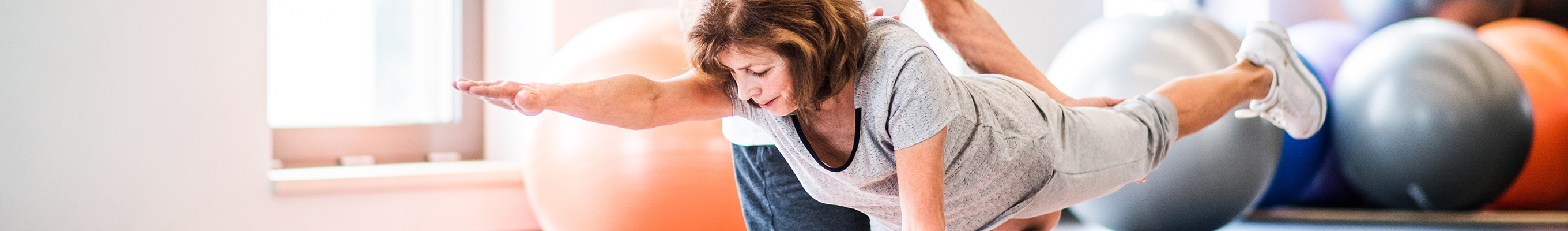 Frau macht eine Bauchübung auf einer Gymnastikmatte in einem Fitnessraum, große Gymnastikbälle im Hintergrund.