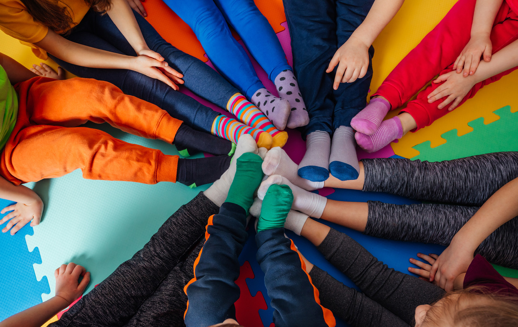 Neun Kinder sitzen im Kreis und strecken die Füße nach vorne zusammen.