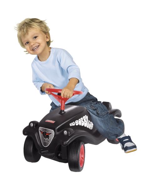 Kleiner Junge fährt fröhlich auf schwarzem Bobby-Car Spielauto mit rotem Lenkrad.