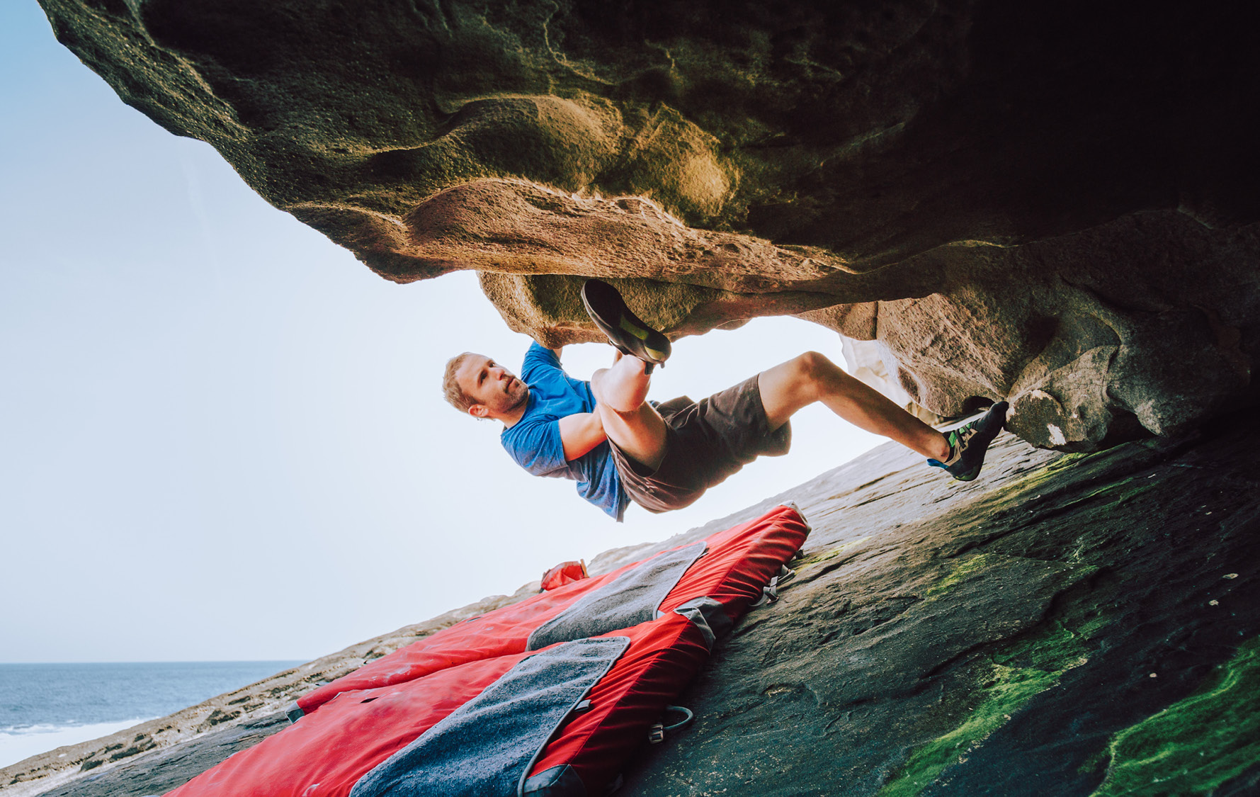 Mann bouldert an Felswand mit einer darunterliegenden Fallschutzmatte (Crashmatte).