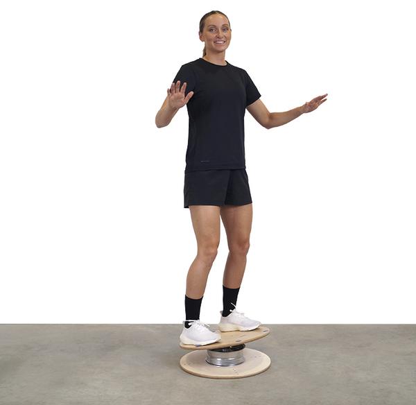 Frau balanciert auf einem runden Balance-Board in Sportkleidung auf grauem Boden.
