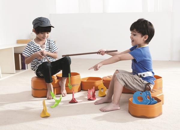 Zwei Jungen spielen mit Angelspiel und bunten Figuren auf orangenen Sitzkissen im hellen Raum.