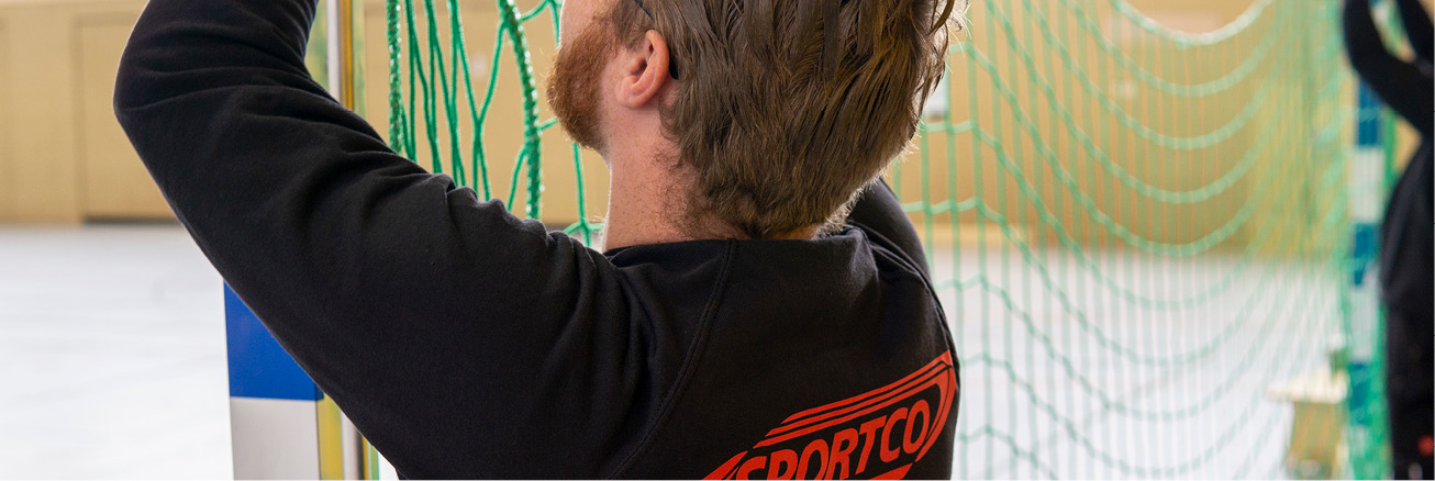 Servicetechniker von SPORTCO bei der Montage bzw. Befestigung eines Tornetzes in einer Sporthalle.