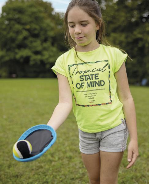 Mädchen spielt mit Ball und Schläger im Park an einem sonnigen Tag.
