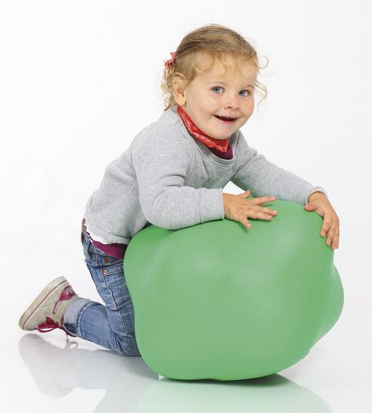 Kleines Mädchen spielt lachend mit großem grünen Ball auf weißem Hintergrund.