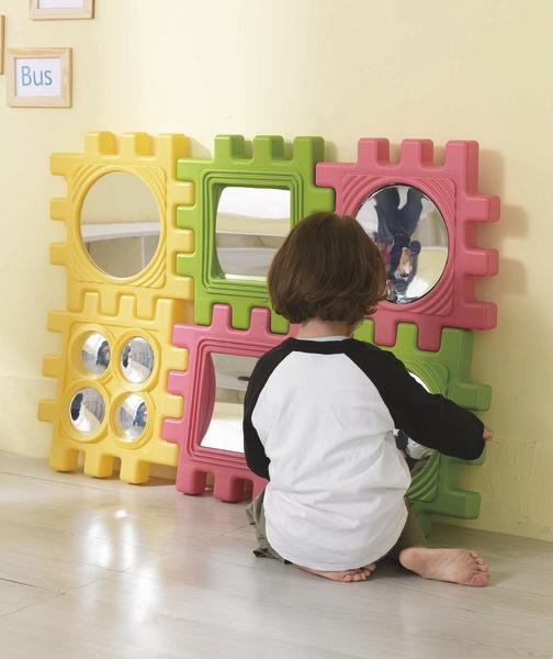 Kind spielt mit bunten Spiegelbausteinen an der Wand in einem hellen Raum.